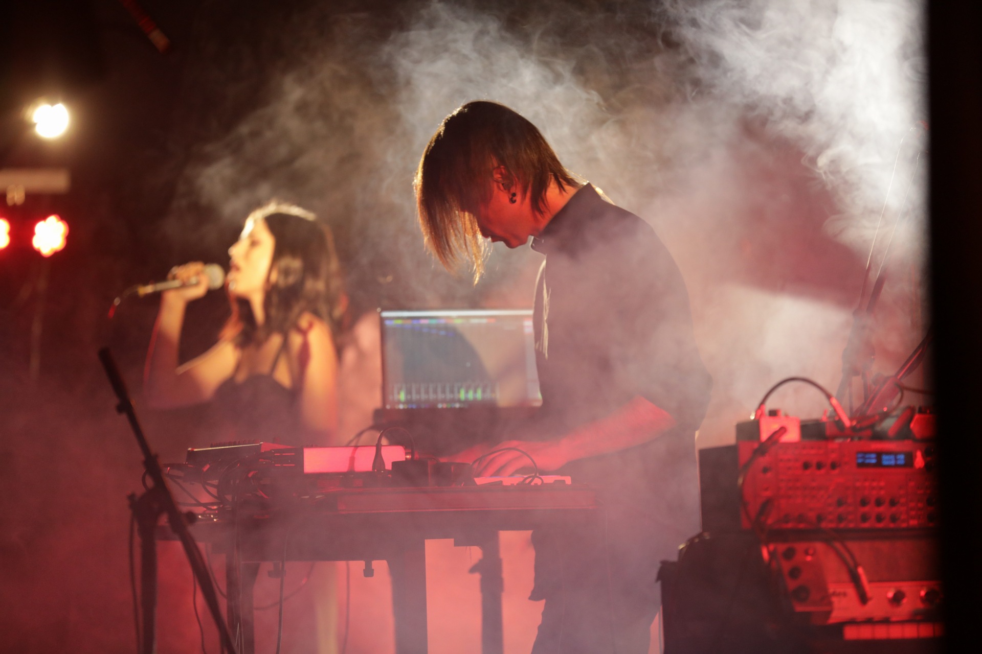 Μέσα σε καπνούς και τυλιγμένοι σε πορτοκαλοκόκκινο φώς, ένας άντρας με τσουλούφι ντυμένος στα μαύρα παίζει μουσική σε πλήκτρα και synth ενώ στο βάθος μία μελαχρινή κοπέλα τραγουδά στο μικρόφωνο με τα μάτια κλειστά.