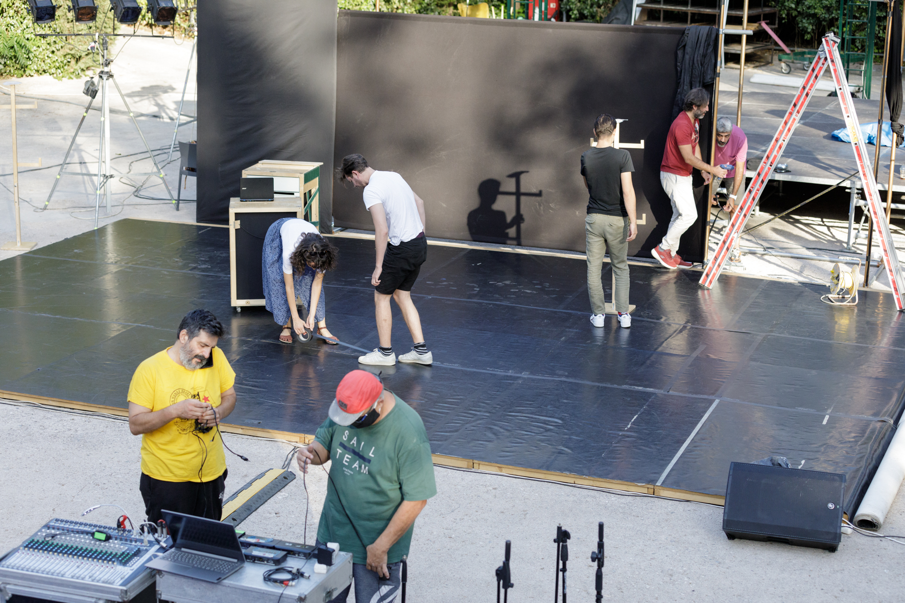 Κάτω από το απογευματινό φως του ήλιου, μία ομάδα ανθρώπων στήνει τη σκηνή του θεάτρου της Ρεματιάς: δύο άτομα σετάρουν την κονσόλα του ήχου, δύο άλλοι κολλούν το πάτωμα από μαύρο λινόλεουμ, κι άλλοι τρεις στο βάθος έχουν στήσει μία σκάλα και περνούν καλώδια.